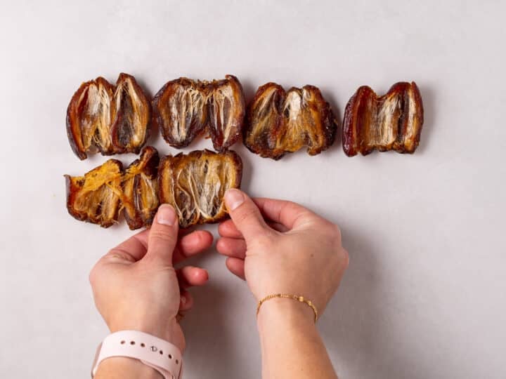 Hands pressing opened dates flat on a sheet of parchment paper