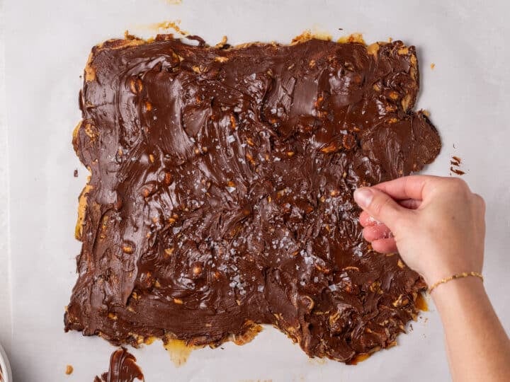 Flaky sea salt being sprinkled over the melted chocolate layer