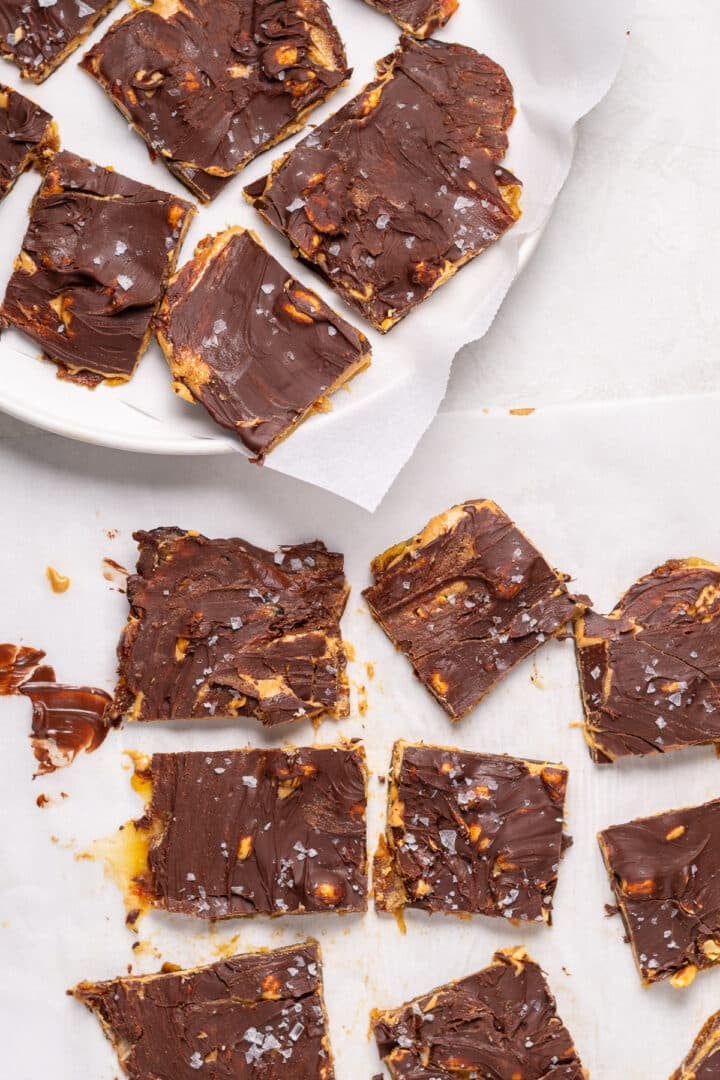 Sliced pieces of snickers date bark topped with melted chocolate, peanuts, and flaky sea salt on parchment paper