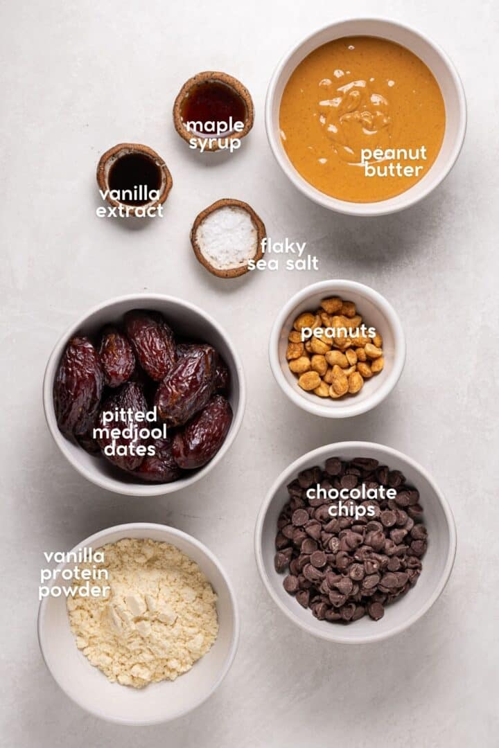 Labeled ingredients for a date bark recipe including dates, peanut butter, chocolate chips, peanuts, maple syrup, vanilla, and flaky salt