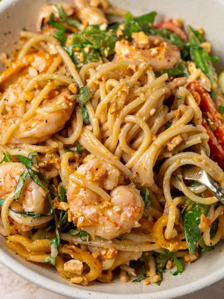Close-up of creamy peanut noodles with shrimp, Thai basil, snap peas, and crushed peanuts