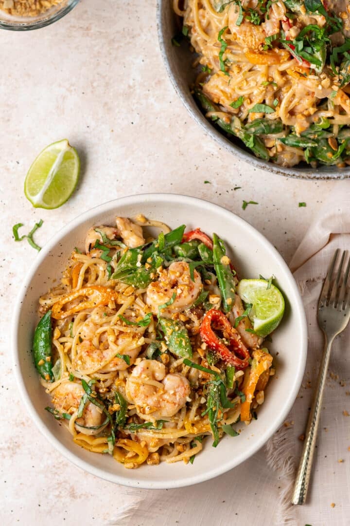Plated peanut noodles with shrimp topped with Thai basil, green onions, and crushed peanuts