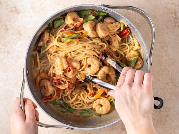 Tossing shrimp peanut noodles with snap peas and mini peppers in creamy peanut sauce