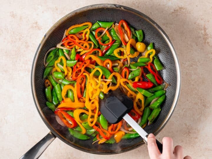 Snap peas, mini peppers, and shallots sautéing in black skillet