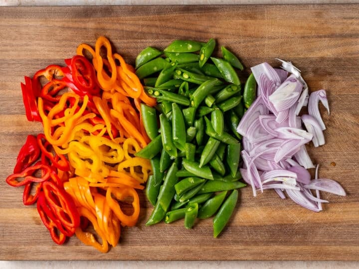 Sliced mini peppers, snap peas, and shallots prepared for peanut noodles with shrimp