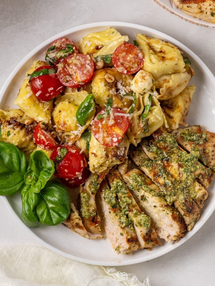 portion of tortellini caprese salad plated with sliced pesto chicken breast