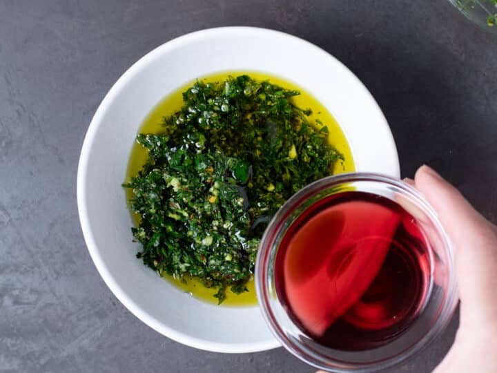 hand pouring red wine vinegar in to bowl with olive oil and fresh cilantro and parsley