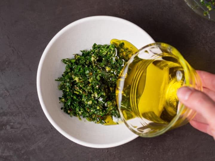 hand pouring olive oil into bowl with fresh herbs