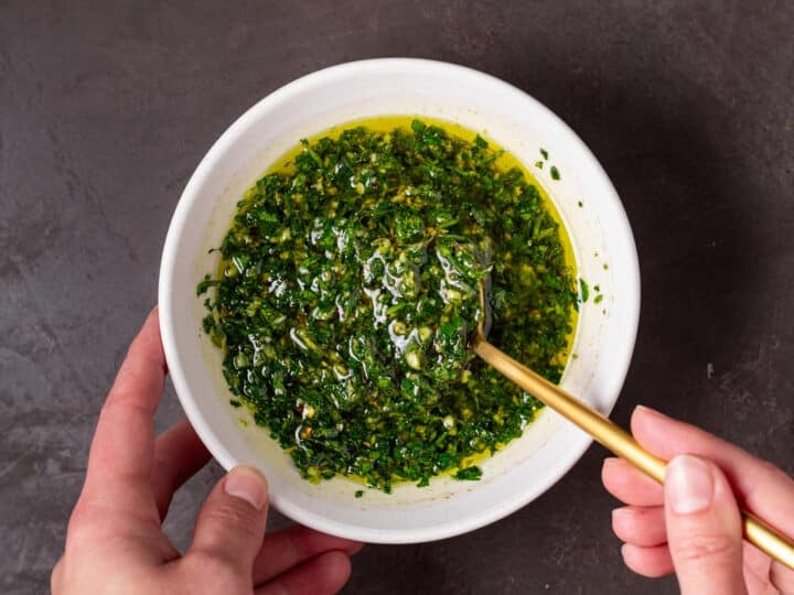 hand using a gold spoon to mix together cilantro chimichurri