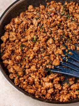 Close-up of saucy garlic ginger ground chicken in a skillet with fresh herbs and sesame seeds.
