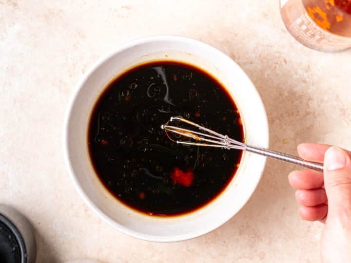 Honey, coconut aminos, sesame oil and sriracha being whisked together in a small bowl.