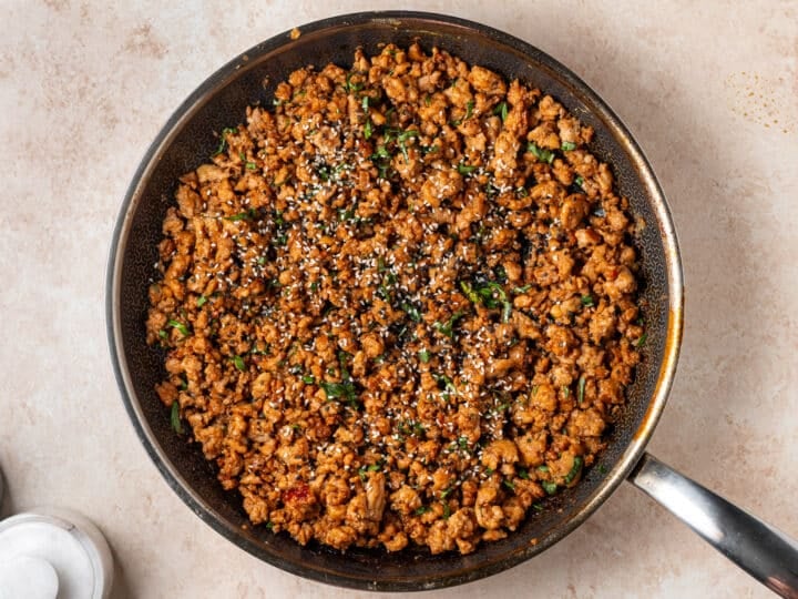 Finished ground chicken in a skillet topped with sliced Thai basil and sesame seeds.