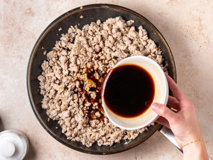 Sauce being poured over cooked ground chicken in a skillet.