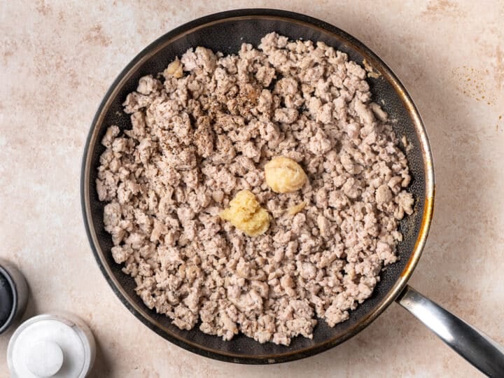 Cooked ground chicken in a skillet with garlic paste, ginger paste, salt and pepper.