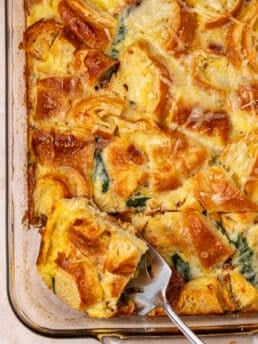 spatula removing a slice of egg casserole topped with croissants and cheese