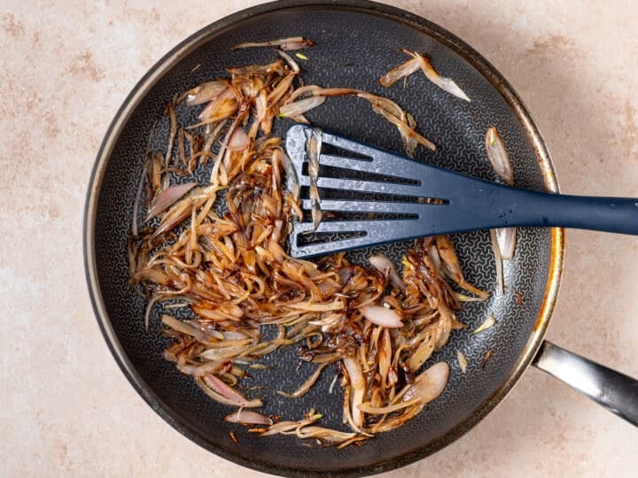 black skillet with caramelized shallots and a spatula stirring them