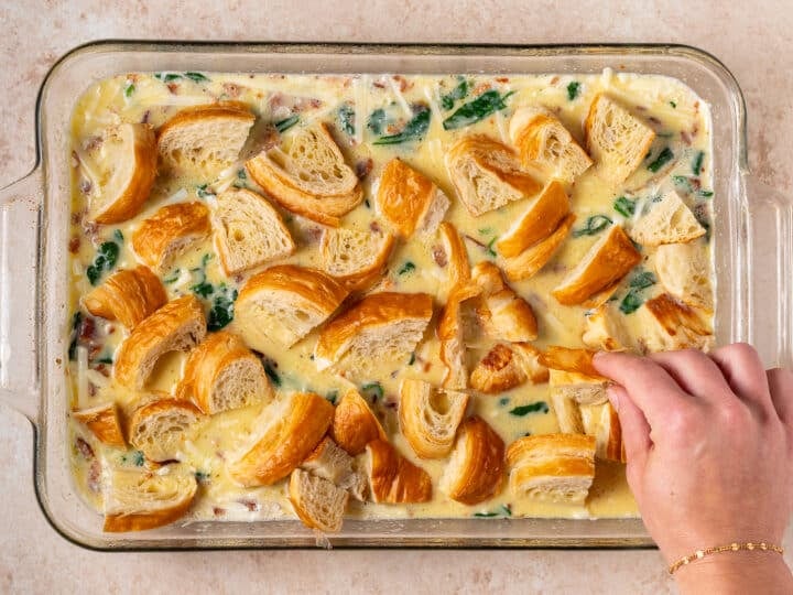 hand placing croissant pieces on top of egg casserole