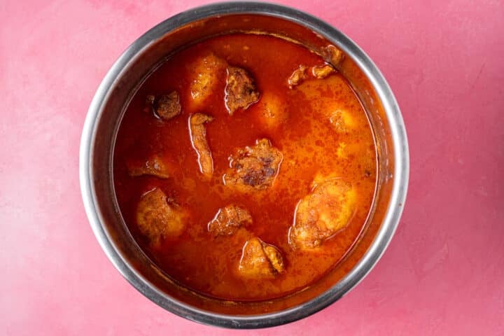 Cooked chicken thighs braising in flavorful cooking liquid.