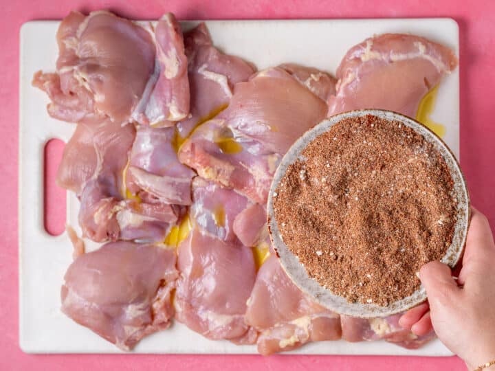 Smoky spice rub getting sprinkled on raw chicken thighs.