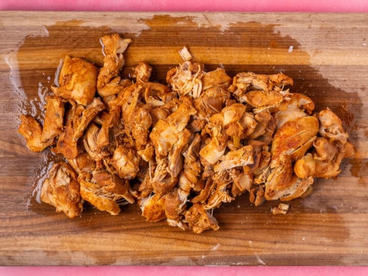 Cooked chicken thighs laid out on wooden cutting board.