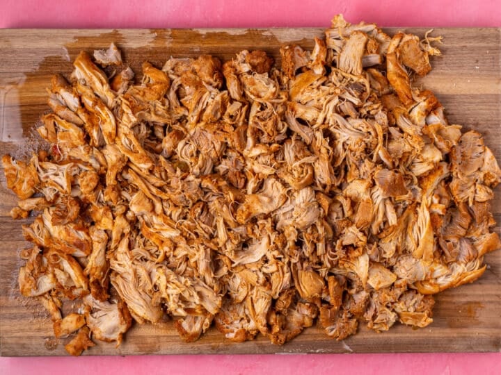 Cooked chicken being roughly shredded on a cutting board.