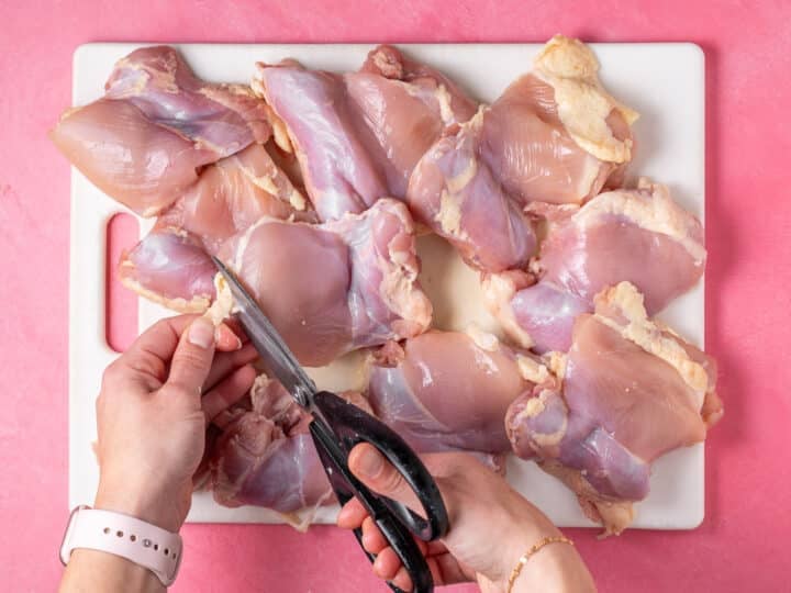 Trimming excess fat from chicken thighs with kitchen scissors.