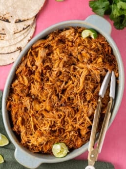 Smoky shredded chicken piled in a serving dish with tortillas and fresh lime wedges on the side.