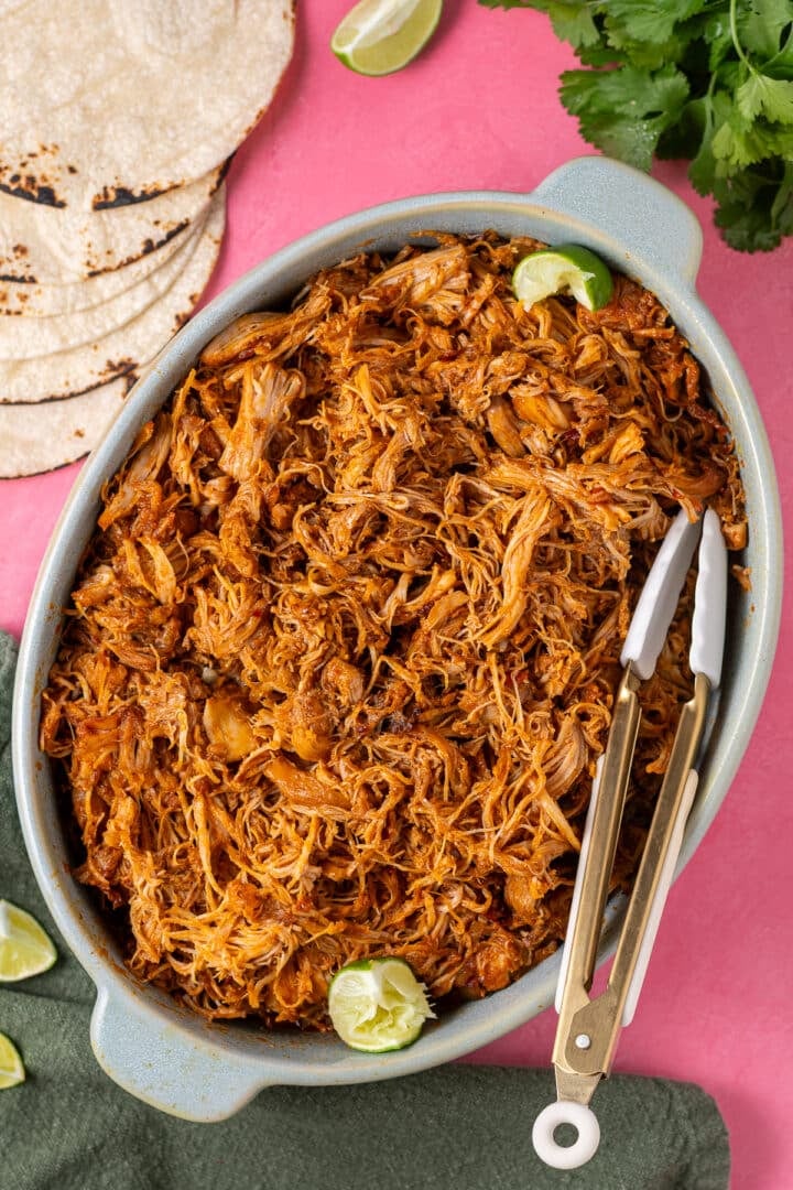 Smoky shredded chicken piled in a serving dish with tortillas and fresh lime wedges on the side.