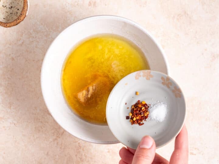 Red pepper flakes and salt being added to a bowl with oil, miso paste, garlic, ginger and mirin.