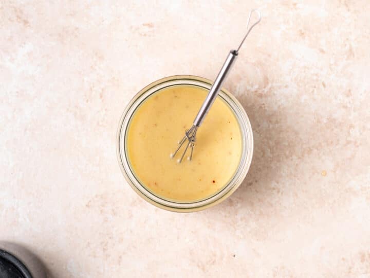 Creamy dressing in a mason jar with a mini whisk.