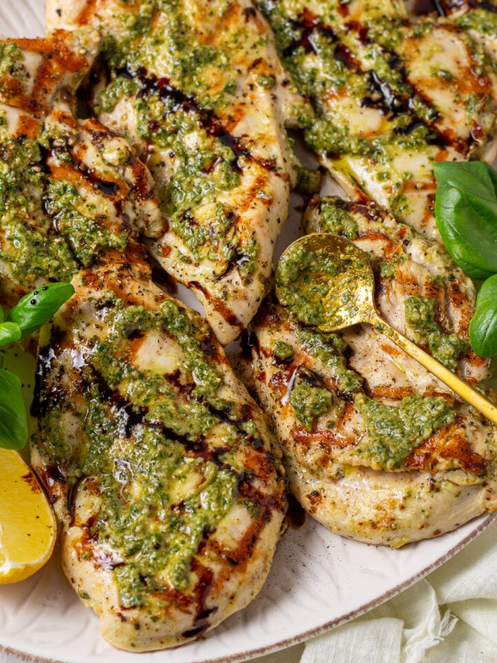 Close-up of grilled pesto chicken with basil pesto, balsamic glaze, lemon, and fresh basil