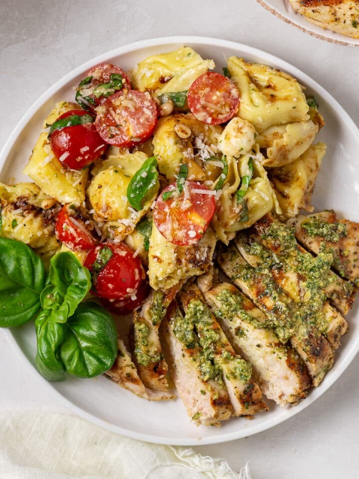 close up view of sliced chicken with pesto, tortellini salad with tomatoes and fresh basil