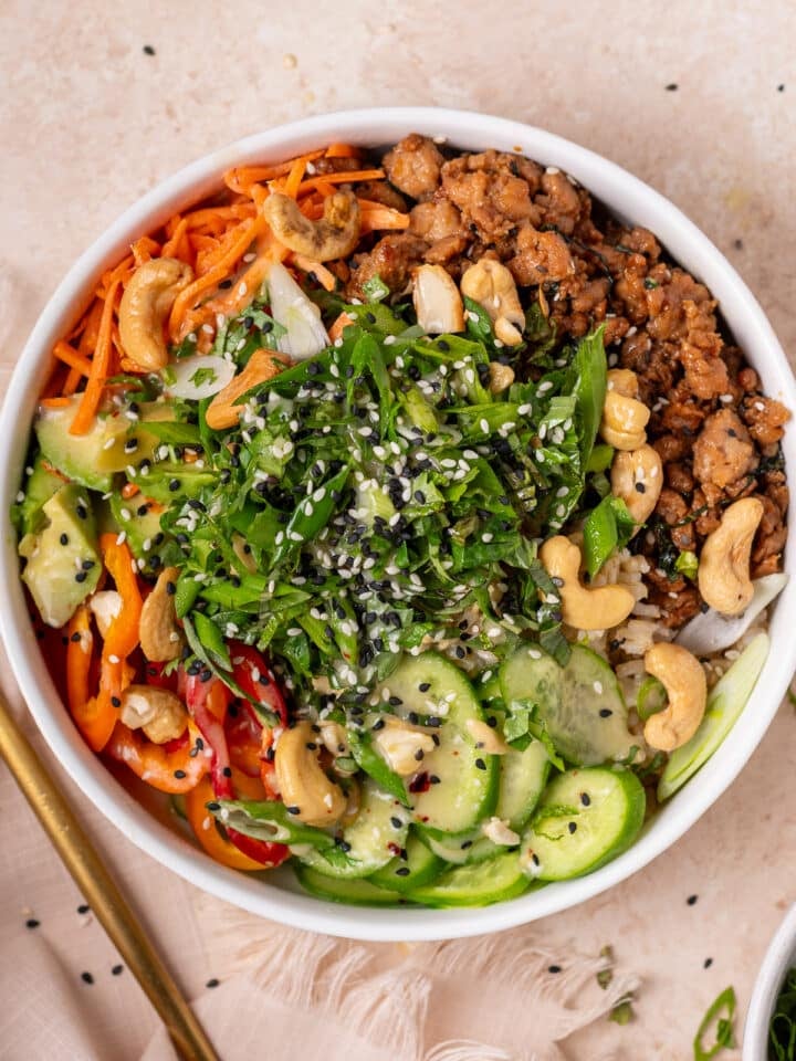 Assembled power bowl topped with fresh herbs, cashews, cucumbers, sesame seeds, chicken and brown rice.