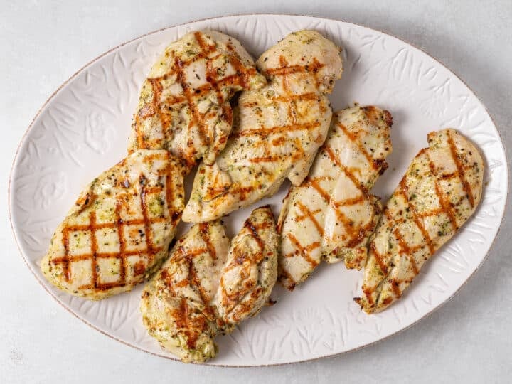 Grilled chicken breast with golden hatch marks resting on a white platter