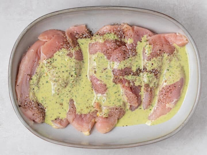 Raw chicken breast seasoned with salt and pepper and drizzled with pesto vinaigrette