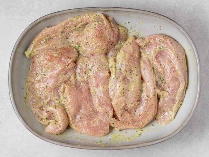 Raw chicken cutlets tossed with creamy pesto marinade in a shallow dish