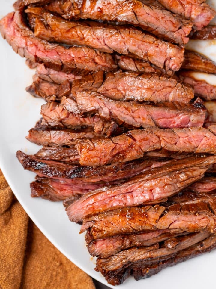 Close up of grilled skirt steak on a white platter with juicy pink center.