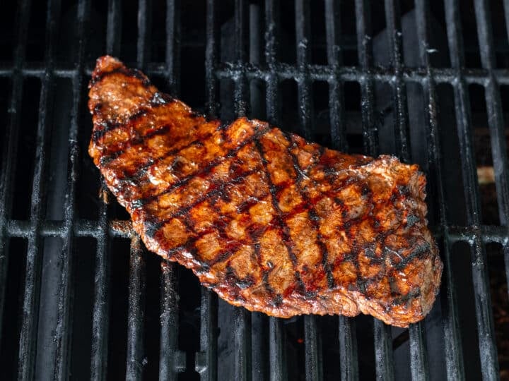 Skirt steak with charred grill marks on grill grates.