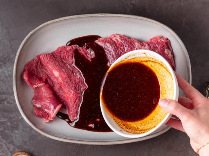 Pouring marinade over raw skirt steak in a shallow dish.