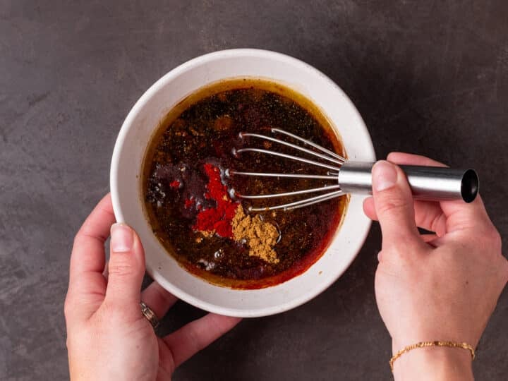 Balsamic vinegar, olive oil, soy sauce, Worcestershire, garlic and spices whisked together in a small white bowl.
