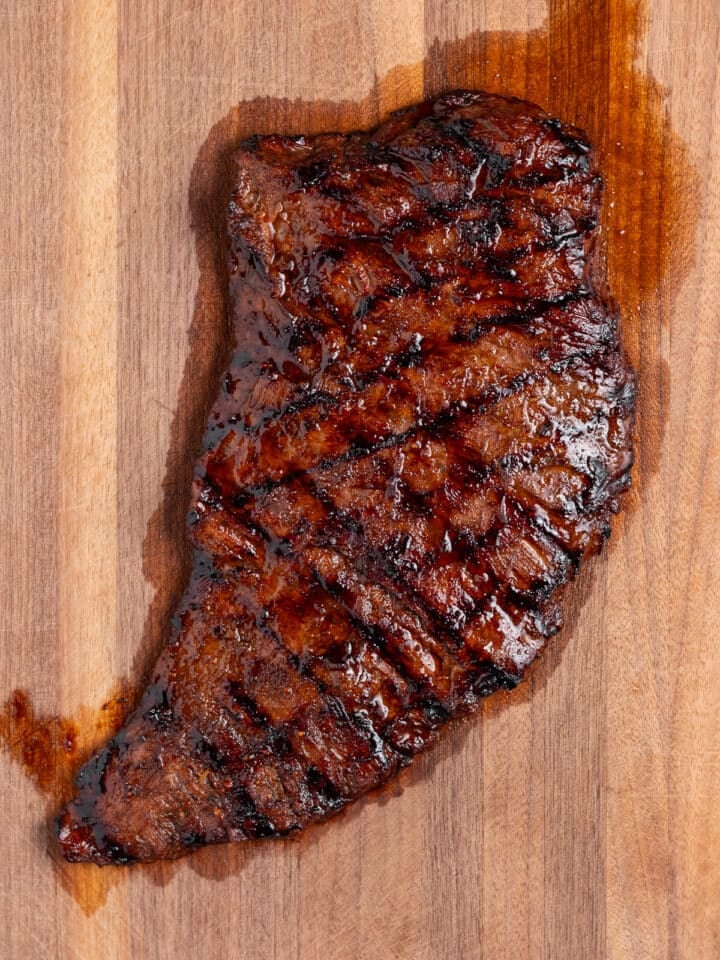 Rested grilled skirt steak on a wooden cutting board with caramelized edges and grill marks.