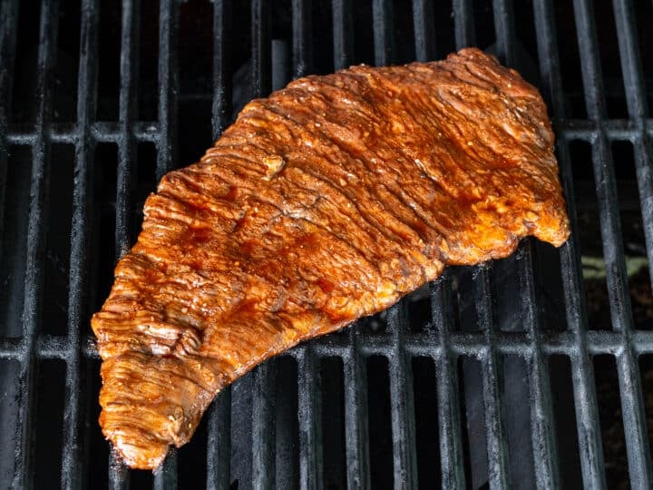 Marinated skirt steak placed on hot grill grates to cook.