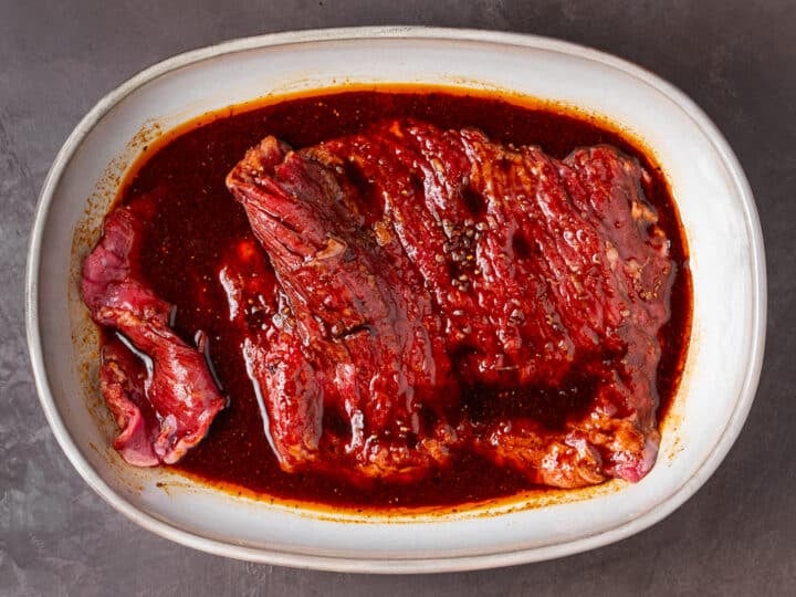 Skirt steak soaking in a smoky marinade in a dish.