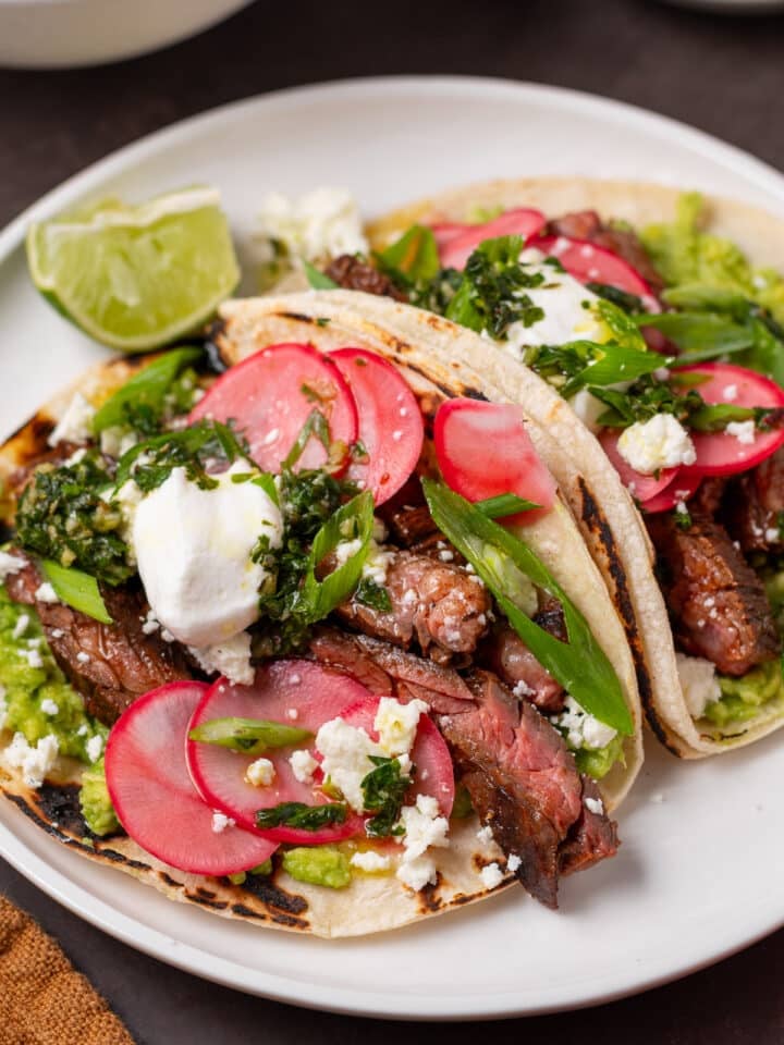 Close-up of skirt steak tacos with pickled radishes, avocado, queso fresco, sour cream and fresh chimichurri.