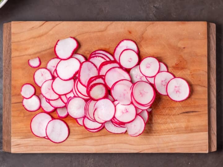 Thinly sliced radishes on a wooden cutting board.