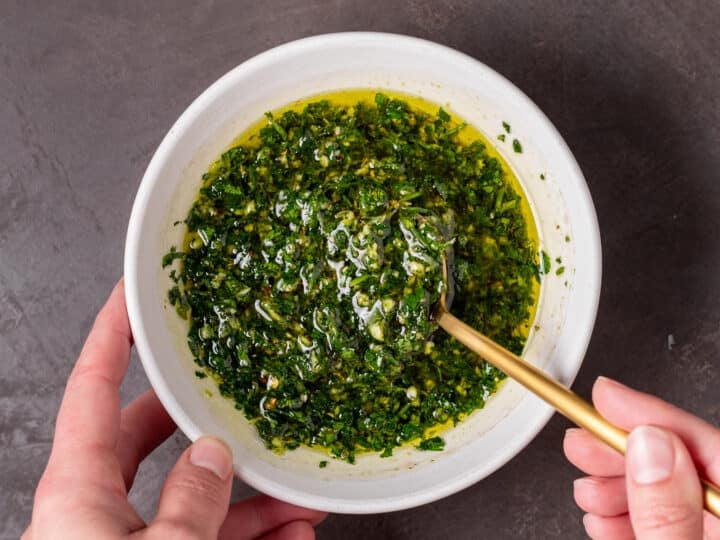 Cilantro chimichurri sauce in a white bowl being stirred with a gold spoon.