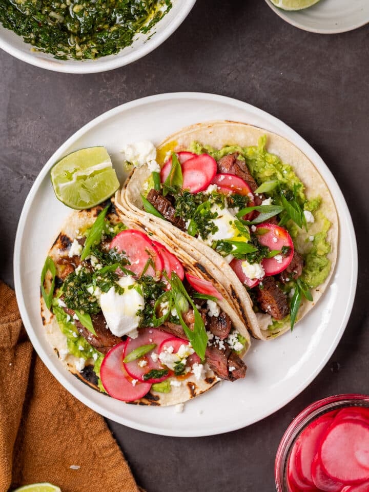 Skirt steak tacos topped with avocado, pickled radishes, queso fresco, green onions and chimichurri.