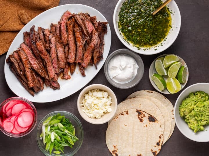 Sliced grilled skirt steak with tortillas, mashed avocado, sour cream, queso fresco, lime wedges, pickled radishes, green onions and cilantro chimichurri.