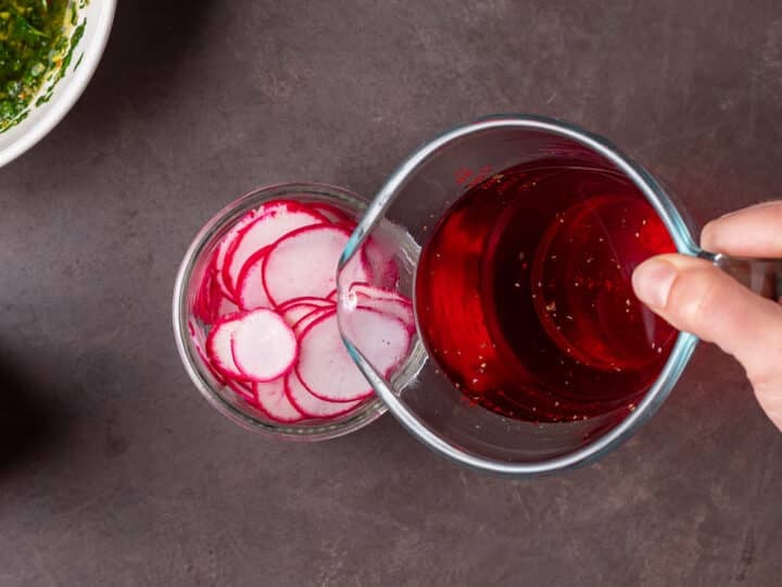 Quick-pickled radish brine being poured over thinly sliced radishes in a jar.