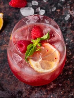 Pink gin spritz with raspberries, fresh basil and a lemon slice served over ice